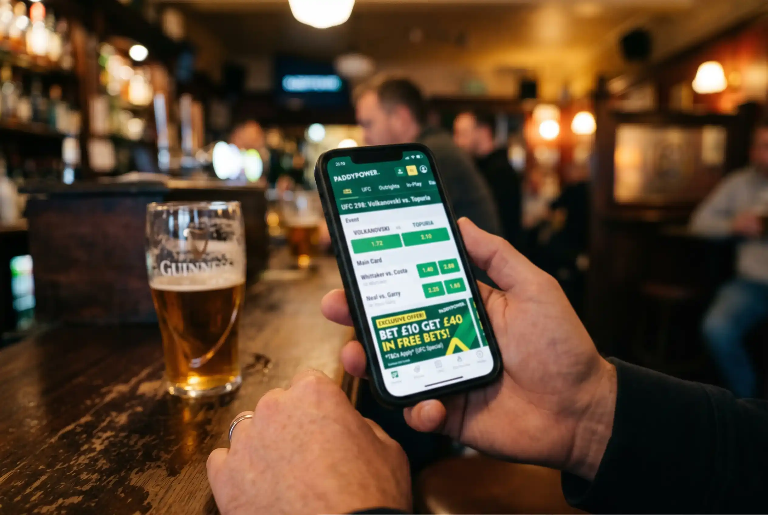 Mobile phone showing UFC odds and promotional banners on a sportsbook app in a pub setting