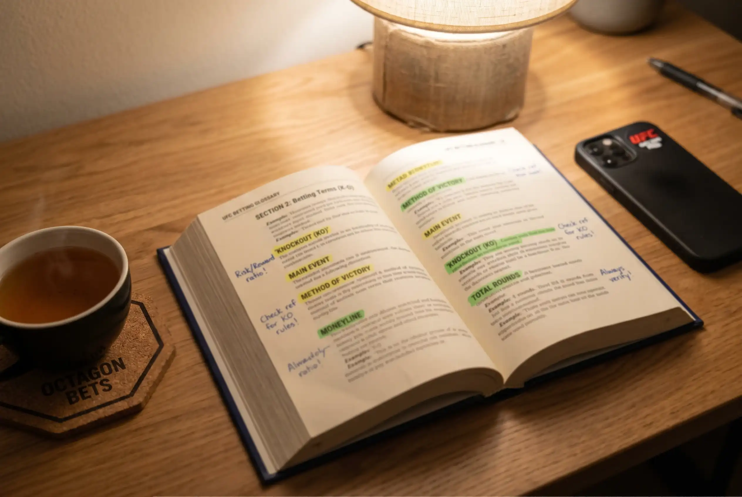 Open reference book with UFC betting terms highlighted next to an octagon-shaped coaster on a desk