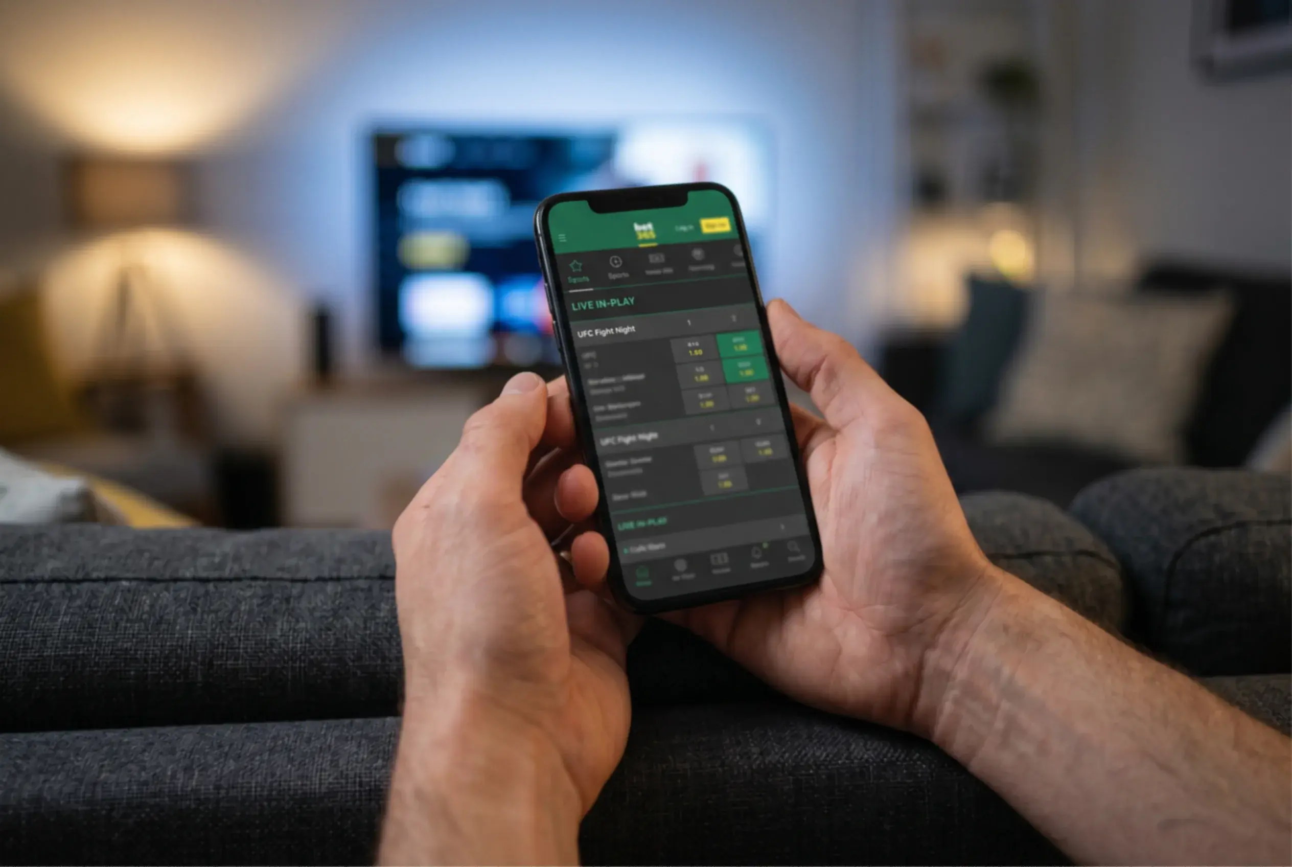Hands holding a smartphone displaying a sports betting interface during a live UFC event